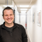 A man smiling for a photo in a corridor.