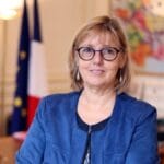 A profile photo of a woman, she is blonde and wearing glasses and a blue jacket.